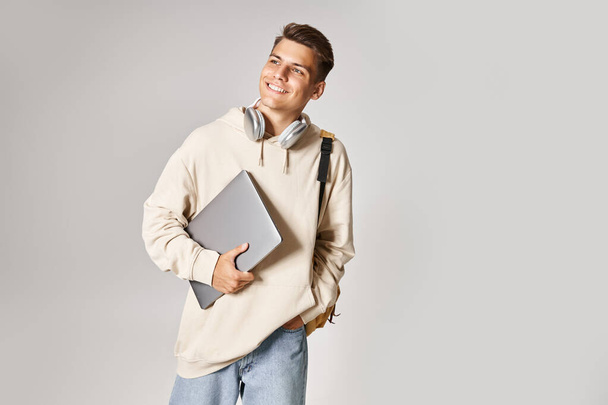 charming student in his 20s with laptop and headphones walking and looking to side - Fotó, kép