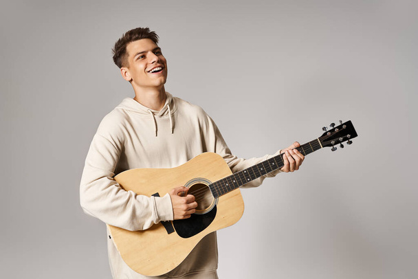 atractivo hombre de 20 años con cabello castaño tocando la guitarra sobre fondo claro - Foto, Imagen