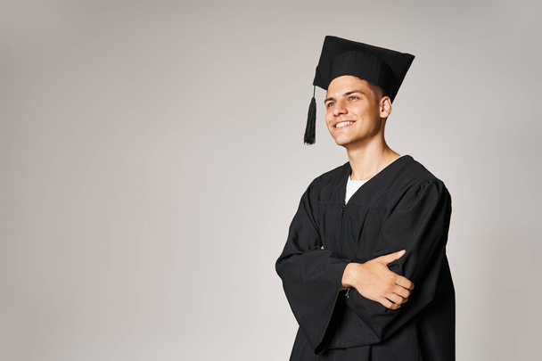 retrato de estudiante atractivo en vestido de graduado y gorra sonriendo y mirando hacia adelante - Foto, imagen