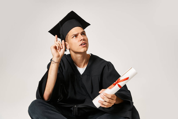 attractive young student in graduate outfit came up with idea against grey background - Photo, Image