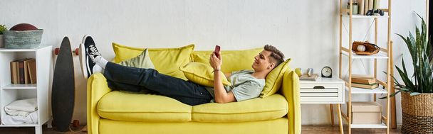 vízszintes lövés fiatal férfi feküdt sárga kanapén a nappaliban, és görgetés a szociális média - Fotó, kép