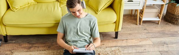 baner studenta ze słuchawkami i laptopem na podłodze przy żółtej kanapie w notatce - Zdjęcie, obraz