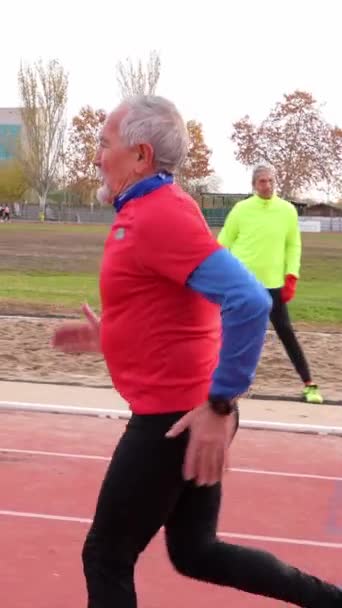 Vanhempi Valkoihoinen miehet punaisissa urheiluvaatteissa käynnissä raiteilla, esittelee terveyttä ja kestävyyttä - Materiaali, video