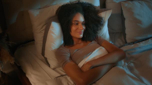 Tranquillo rilassato donna afro-americana bella ragazza sdraiata in camera da letto buio riposo notturno sogni dolci ricreazione sorridente sognando femminile rilassarsi in accogliente comodo letto materasso cuscino ortopedico - Filmati, video