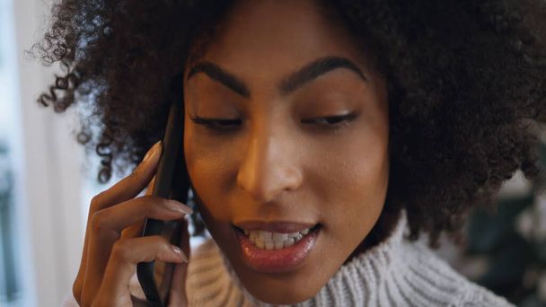 Positive woman calling smartphone at home close up. Curly smiling lady talking friend discussing news at evening interior. African friendly girl sharing secrets at cellphone call. People lifestyle - Photo, Image