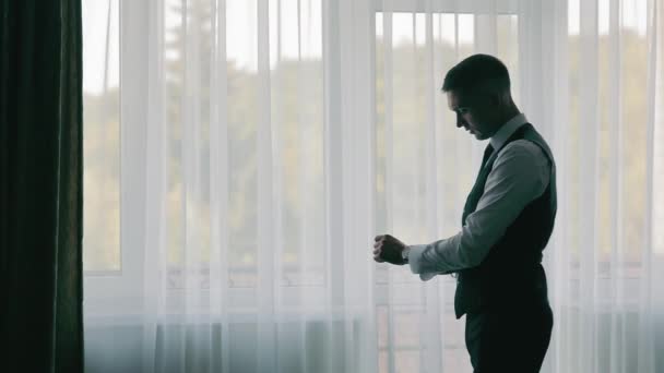 Gentleman Preparing for Event, Silhouette eines Mannes im Anzug, der seinen Ärmel an einem Fenster mit blanken Vorhängen justiert - Filmmaterial, Video