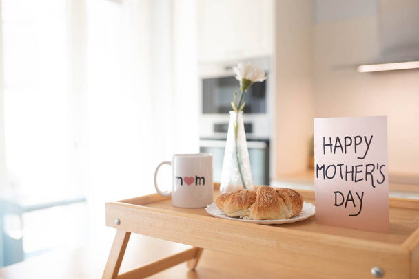 Bodegón del día de la madre con taza de mamá, una pastelería dulce y una tarjeta de felicitación en una bandeja, en un fondo interior aireado. - Foto, Imagen
