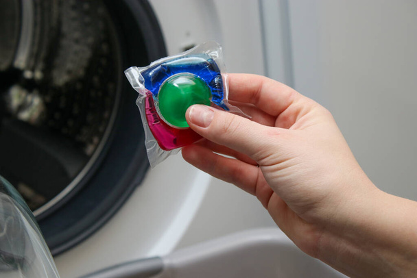 Großaufnahme einer Frauenhand, die eine bunte Waschgelkapsel in die Waschmaschine legt - Foto, Bild