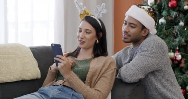 Phone, online shopping and couple at Christmas in home with choice of gift and discussion of holiday. Happy, people and relax with smartphone, app or talking about ecommerce sales and discount. - Footage, Video