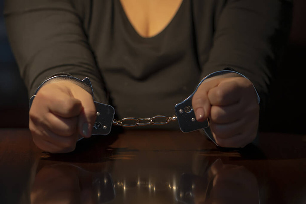 手錠をかけられた女性の手がテーブルの上に横たわっている. コンセプト:尋問と拘留,調査と証言. - 写真・画像
