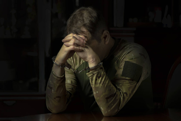 Um soldado militar solitário, algemado, escondendo o rosto, num quarto escuro. Conceito: prisão e interrogatório, testemunhando a um investigador. - Foto, Imagem