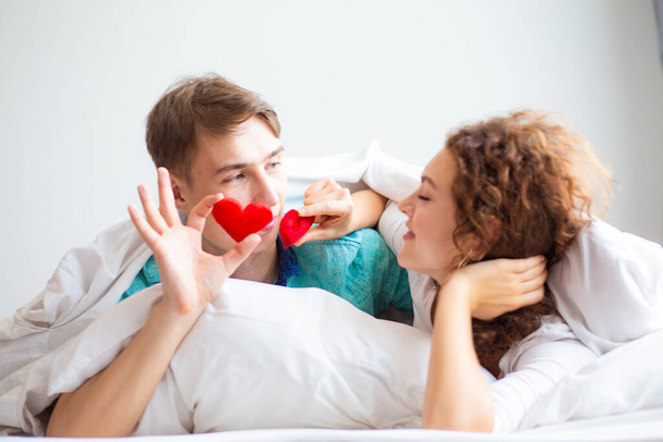 Ερωτικό ζευγάρι ξαπλωμένο σε λευκό κρεβάτι κουβέρτα κρατήστε το σύμβολο της καρδιάς Valentine έννοια - Φωτογραφία, εικόνα