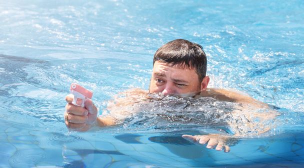 Мужчина играет с водяным пистолетом в бассейне на отдыхе - Фото, изображение