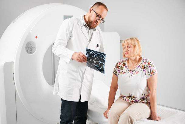 医学の計算されたトモグラフィーかMRIスキャナー. MRIを作成する患者,医師は,結果を保持し,説明します. ソファーに座っている女性. 医療・医療に関するコンセプト. - 写真・画像