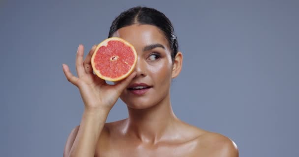 Huid, grapefruit en gezicht van de vrouw op blauwe achtergrond voor welzijn, schoonheid en cosmetica. Dermatologie, spa gezicht en persoon met fruit voor voeding, organische en natuurlijke voordelen in de studio. - Video