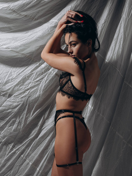 Mladá sexy svůdná žena pózující v krajkové černé spodní prádlo a suspendový pás v tmavém studiu na šedém pozadí. BDSM styl. Detailní záběr. Zadní pohled. - Fotografie, Obrázek
