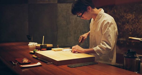 Japoński kucharz, restauracja i cięcia ryb na sushi, okulary i precyzja z nożem do zdrowej żywności w kuchni. Azjata, ręce i kulinarny artysta w pracy przez deskę do drewna, stół i surowe owoce morza menu. - Zdjęcie, obraz