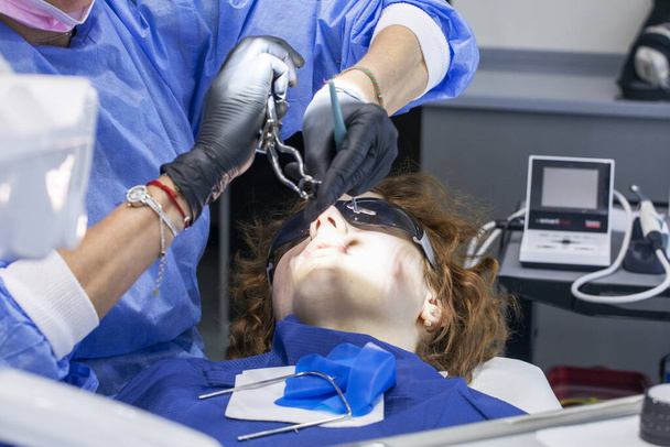 meisje op de tandarts bank dragen zonnebril tijdens tandheelkundige behandeling - Foto, afbeelding