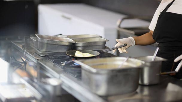 Close-up de cozinheiro prepara omelete em frigideira na cozinha, cozinhar em cafés e restaurantes. Chef profissional fazendo sobremesa, almoço à venda. Conceito alimentar - Foto, Imagem