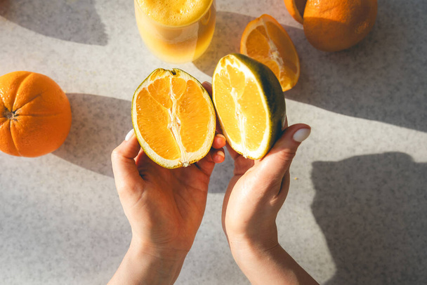Las mitades de una naranja fresca en manos femeninas en el fondo de la mesa de la cocina, vista superior. Preparación de zumo natural en casa. - Foto, imagen