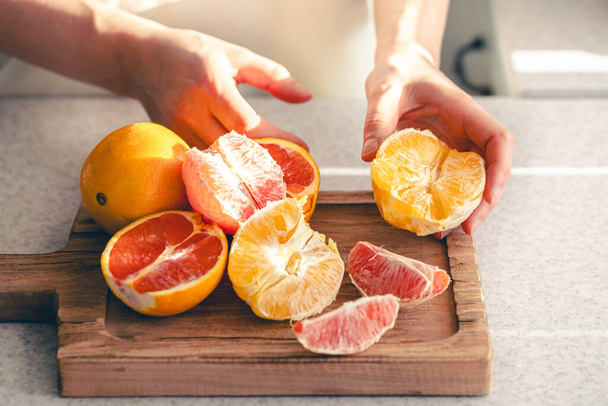 Kadın ellerinde soyulmuş portakallar ve meyve suyu için tahta kesme tahtasının üzerinde. Ev mutfağında portakal suyu yapma süreci.. - Fotoğraf, Görsel