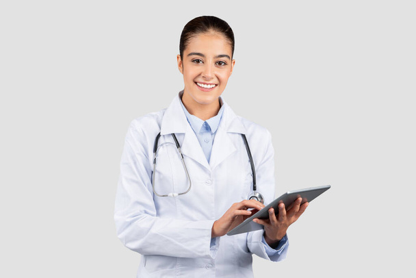 Engaged european doctor in a lab coat and stethoscope using a digital tablet, embodying modern healthcare and the integration of technology in medicine, isolated on gray studio background - Photo, Image