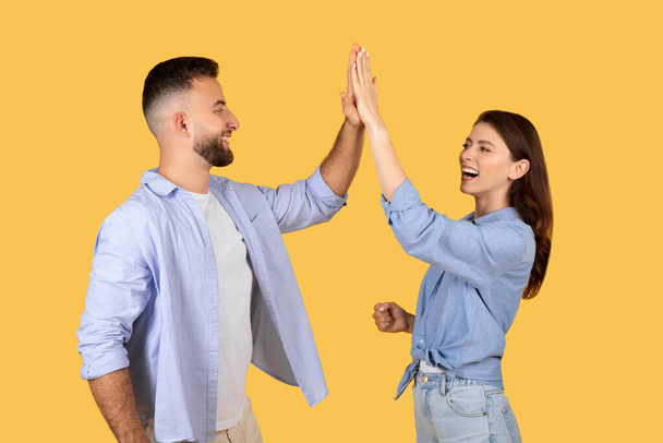 Promieniejący młody mężczyzna i kobieta przybijają piątkę, świętując szczęśliwy moment z poczuciem spełnienia i pracy zespołowej, na wesołym żółtym tle - Zdjęcie, obraz