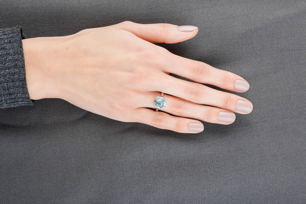 Mooie vrouwelijke hand met gouden ring met diamanten en aquamarijn op grijze achtergrond close-up - Foto, afbeelding
