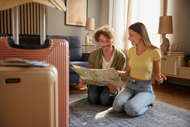 Preparation for vacation concept. Focus on packed luggage suitcases with happy spouses searching travel rout in paper map on blurred background - Photo, Image