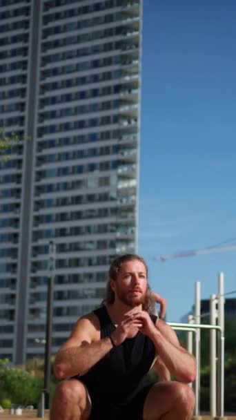 Caucasian athlete man in sportive outfit doing squats while exercising and warming up outdoors at the special place. Fit man bending knees to full squat position - Footage, Video