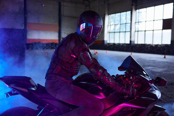 Портрет мотоциклиста в защитном снаряжении и шлеме в неоновом свете. Автодром для обучения в школе вождения - Фото, изображение