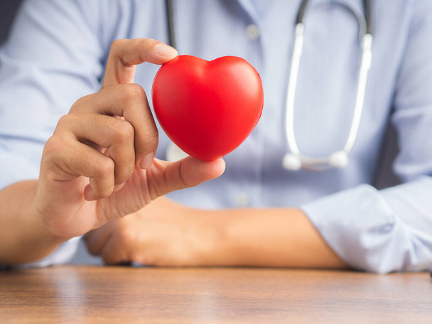 Mão de um médico mostrando uma forma de coração vermelho enquanto sentado no hospital ou clínica. Fotografia de perto. Espaço para SMS. Médico e encorajamento concep. - Foto, Imagem