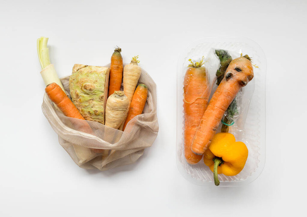 Gemüse vom lokalen Markt in wiederverwendbaren Einkaufstüten und verdorbenes Gemüse in Plastiktüten vor hellem Hintergrund. Ansicht von oben. Bio-Lebensmittel. Umweltverschmutzung durch Plastik, ethischer Konsum. - Foto, Bild