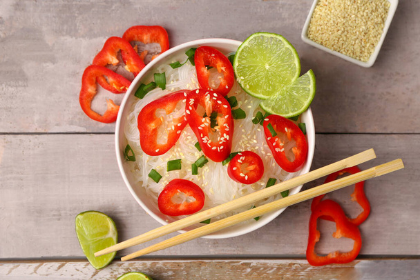 Bowl of tasty rice noodles with bell pepper, lime and sesame seeds on light wooden background - Photo, Image