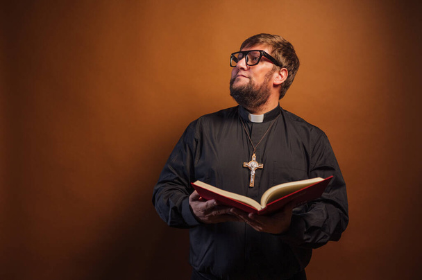 Retrato de un sacerdote con crucifijo y camisa negra sosteniendo una Biblia. - Foto, imagen