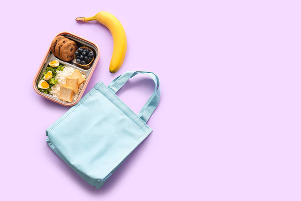 Torba, pudełko śniadaniowe z pysznym jedzeniem i bananem na liliowym tle - Zdjęcie, obraz