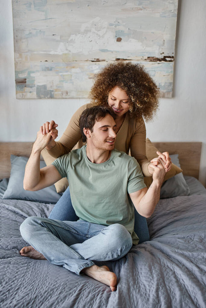 curly young woman and brunette man enjoy a loving hug in their peaceful morning in their cozy bed - Photo, Image