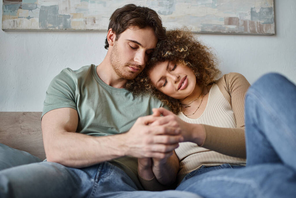 In hun gezellige slaapkamer, gekrulde jonge vrouw en brunette man delen een teander moment en knuffel - Foto, afbeelding