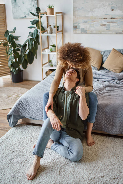 frisée jeune femme étreignant son petit ami par derrière assis sur le lit souriant ensemble - Photo, image