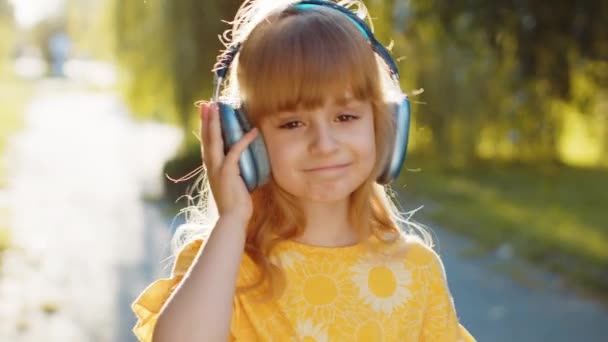 Šťastný nadšený předpubertální dítě v bezdrátových sluchátkách výběru, poslouchat oblíbené energické disco hudby v smartphonu tance. Blondýny legrační dívka s úsměvem na kameru na město západ slunce park - Záběry, video