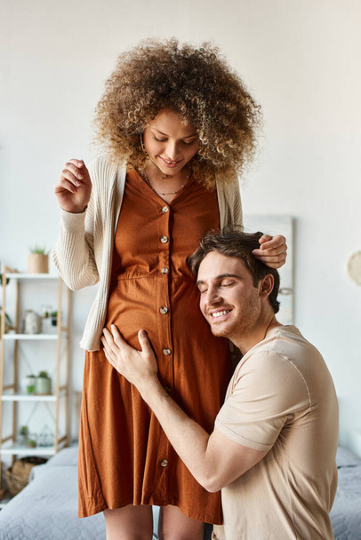 Lovely couple waiting for baby. Handsome smiling happy man listening to baby hugging belly of wife - Photo, Image