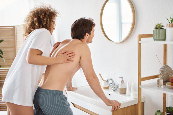 Вид ззаду на кучеряву молоду жінку і брюнетку у ванній, дивлячись у дзеркало, насолоджуючись ранком - Фото, зображення
