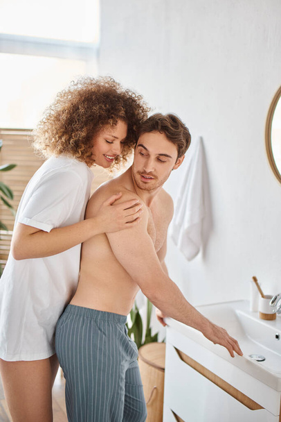 Молодая пара влюбленных обнимает и улыбается друг другу дома в ванной, нежным утром - Фото, изображение