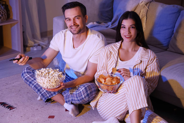 Fiatal pár burgonyaszirmokkal és popcornnal tévézni otthon esténként - Fotó, kép