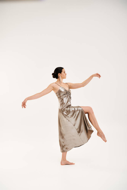 Молодая женщина в серебряном платье изящно танцует в студии, демонстрируя элегантность и движение. - Фото, изображение
