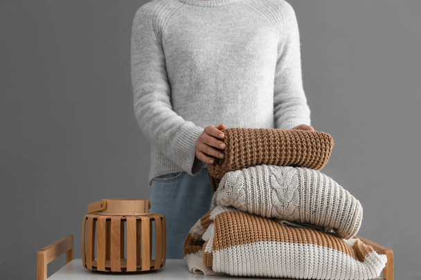 Woman with stack of different stylish sweaters on table near grey wall in room - Photo, Image