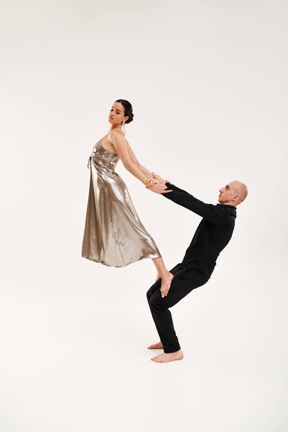 Un jeune homme en noir et une femme en robe argentée exécutent ensemble des mouvements de danse acrobatique sur fond de studio blanc. - Photo, image
