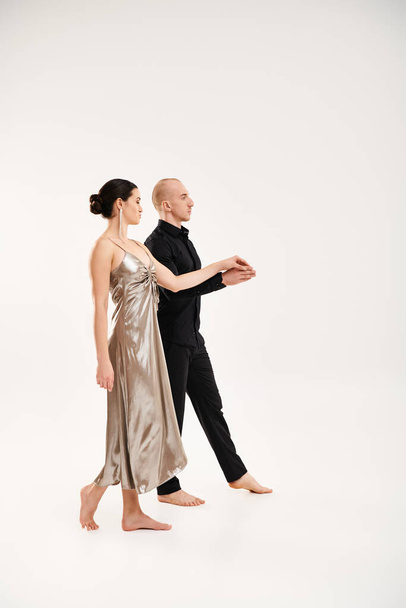 Молодой человек в черном и молодая женщина в серебряном платье танцуют вместе в студии на белом фоне. - Фото, изображение