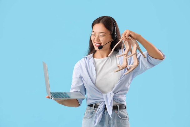 Joven vendedor asiático en auriculares con tacones y portátil sobre fondo azul - Foto, imagen