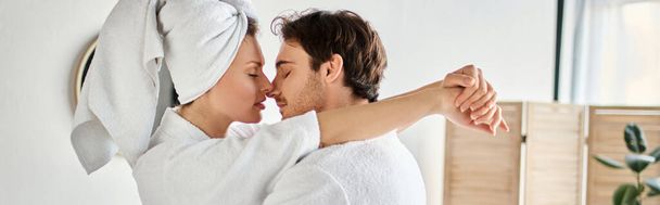 Happy couple in bathrobes kissing in love cuddling in the bathroom, woman with towel on head, banner - Photo, Image